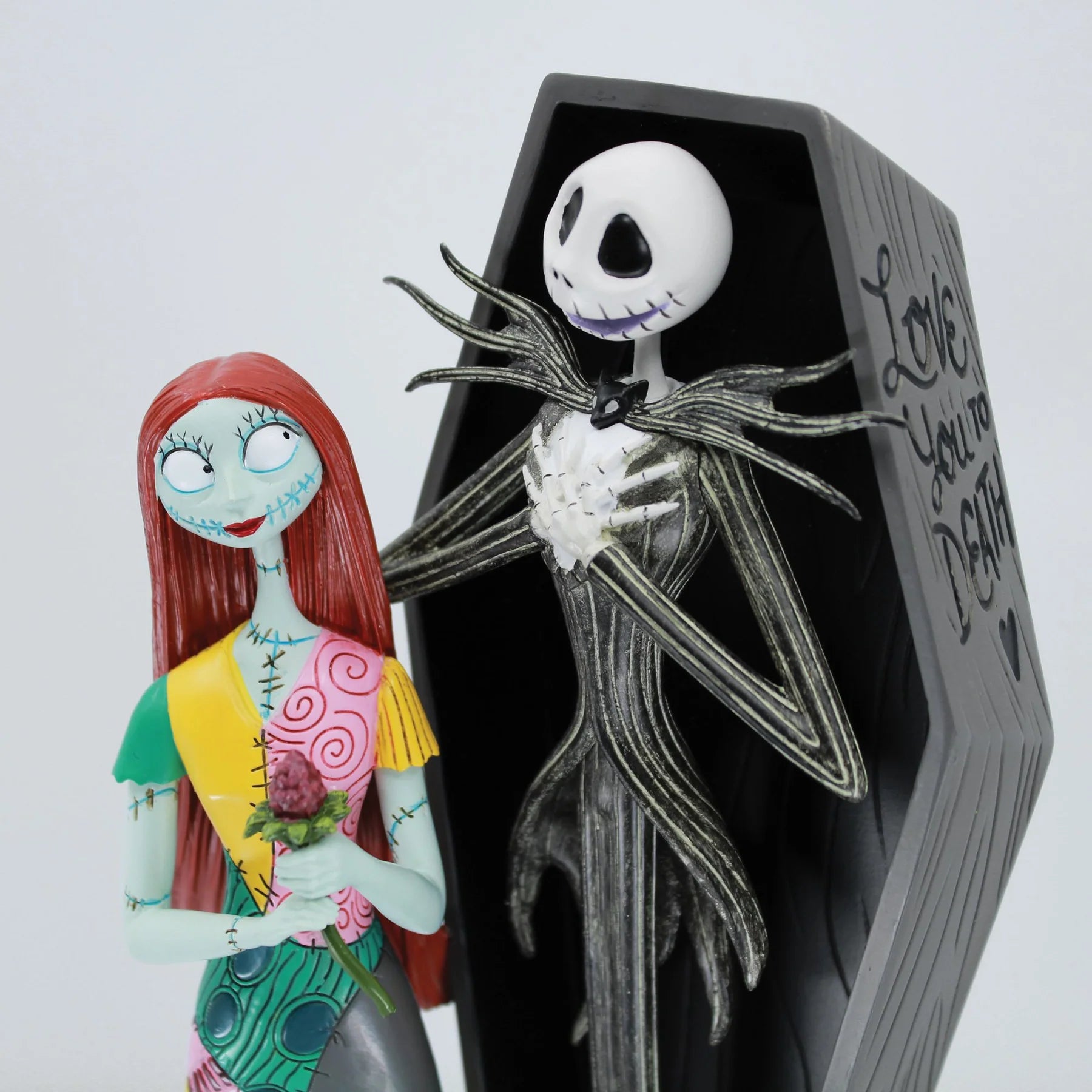 Close-up of the Jack Skellington and Sally Coffin Figurine showing the hand-painted character details and spooky romantic styling from 'The Nightmare Before Christmas' in front of a coffin with text.