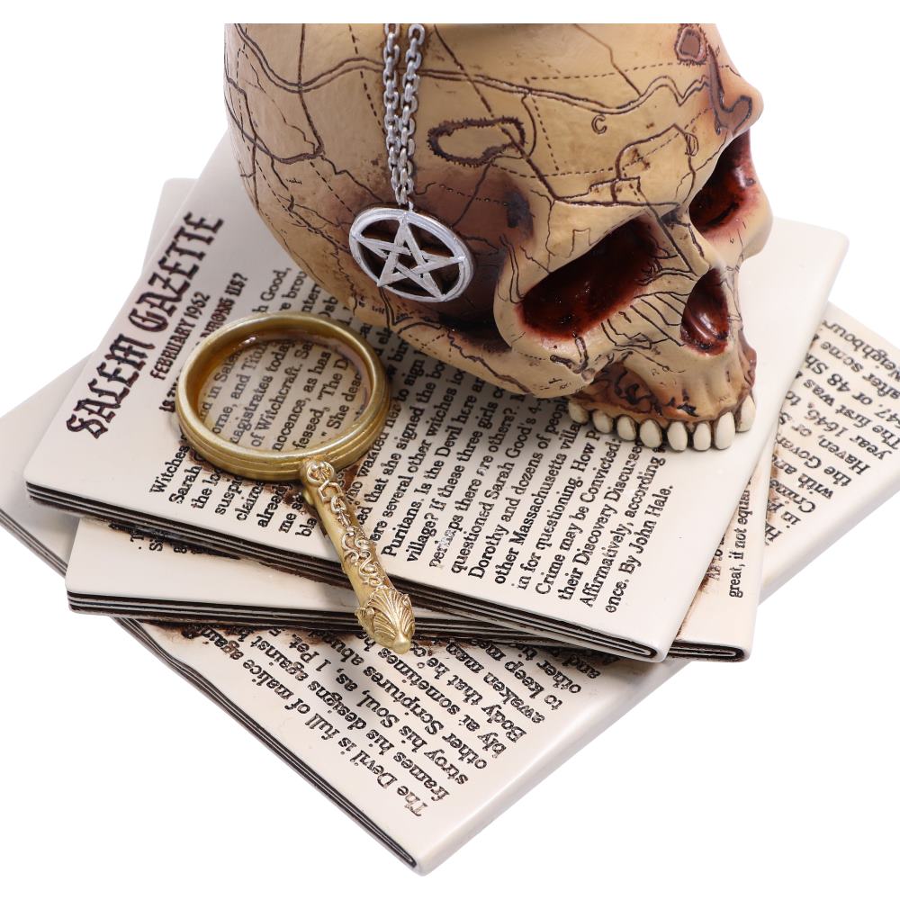 Close-up of the Spirits of Salem Snow Globe base showing the aged newspaper-inspired detailing beneath the skull.