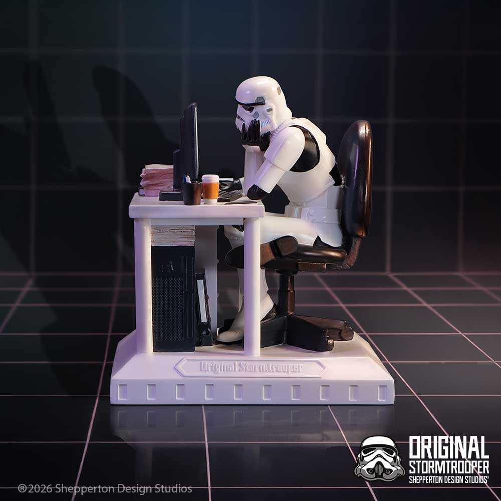 Stormtrooper figure sitting at a desk with a computer, books, and a cup on dislay